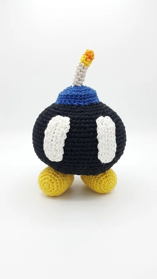 Bob-omb: Eine dunkelblaue runde Figur mit gelben Füßen und einer kleinen Zündschnur. Ansicht 1.